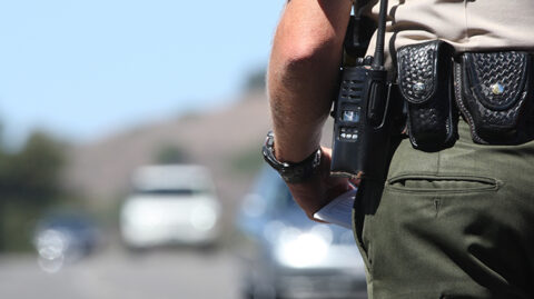 Police officer stepping up to car on highway with ticket