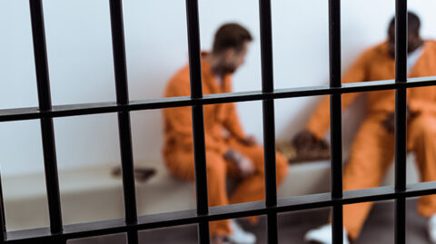 Two men in orange jumpsuits behind prison bars