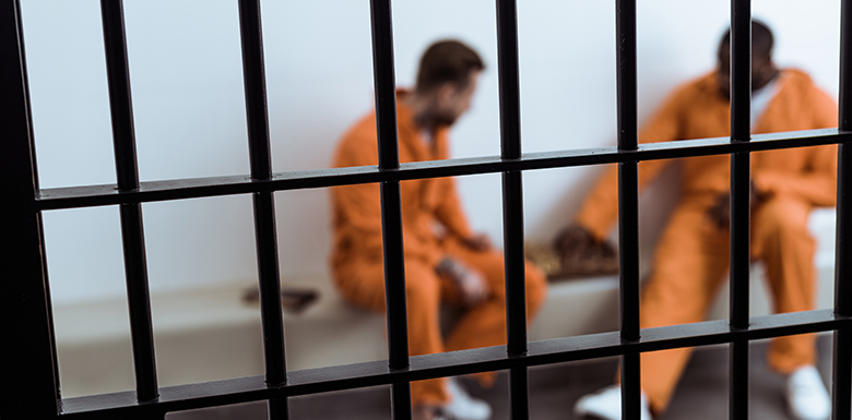 Two men in orange jumpsuits behind prison bars