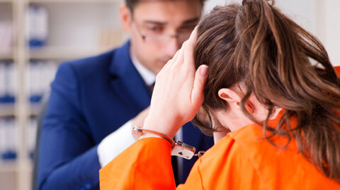 Woman in orange jumpsuit and handcuffs talking to lawyer