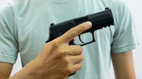 Man holds a gun at chest level, demonstrating gun safety as he discusses the need for a gun for self-defense.