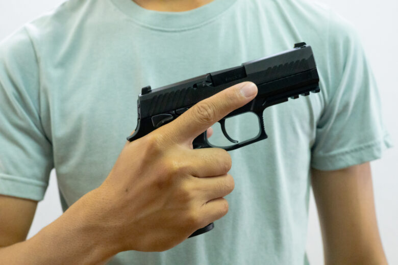Man holds a gun at chest level, demonstrating gun safety as he discusses the need for a gun for self-defense.